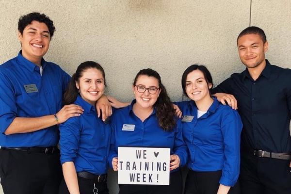 Five uniformed student staff members, one of whom holds a sign that says "We 'heart' training week!"