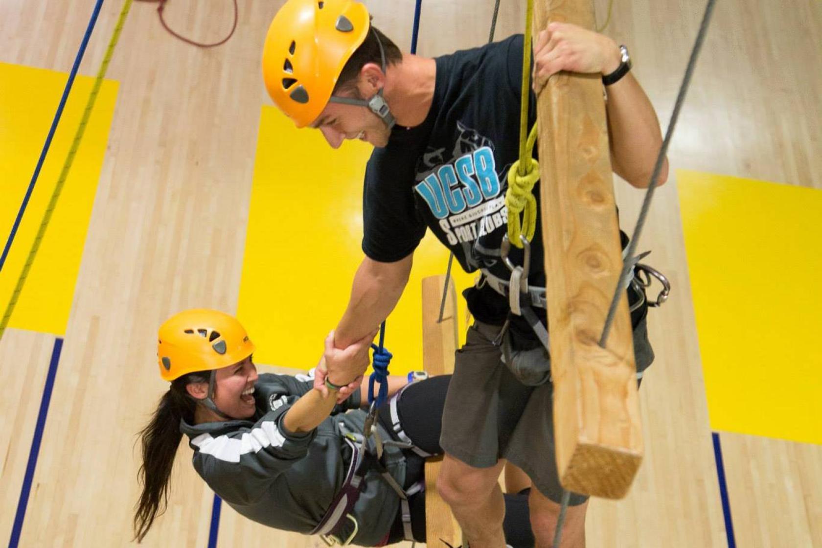 Two people climbing up a ropes course.
